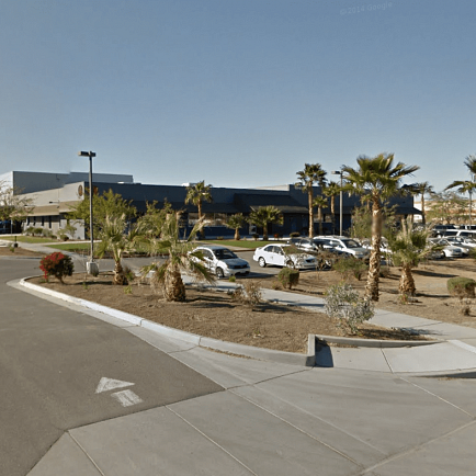 A parking lot featuring palm trees and parked cars under a clear blue sky.